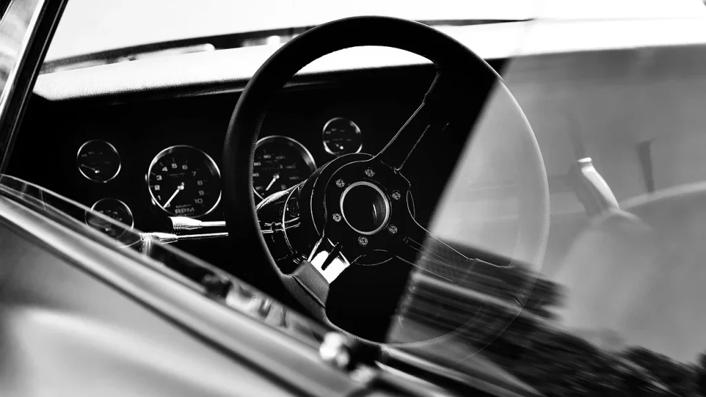 Interior de un coche clásico en blanco y negro, mostrando el volante y el panel de instrumentos con un diseño retro y elegante.