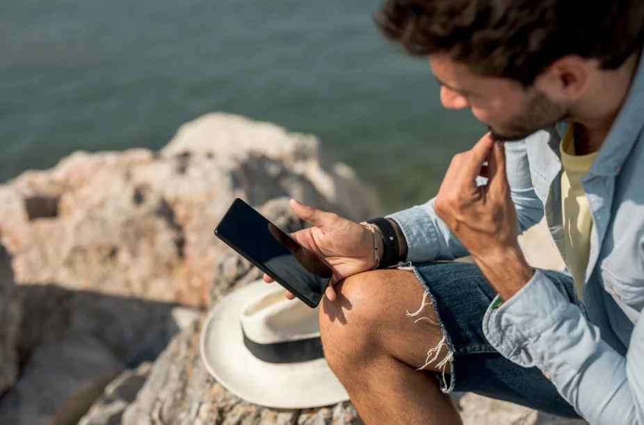 Hombre utilizando su móvil en su viaje cerca del mar para ver sus aplicaciones para viajar al extranjero