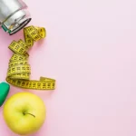 Pesas, cinta métrica, manzana y termo de agua haciendo referencia a la importancia de hábitos saludables que se puede conseguir juntando apps de nutrición y la ayuda de un profesional.