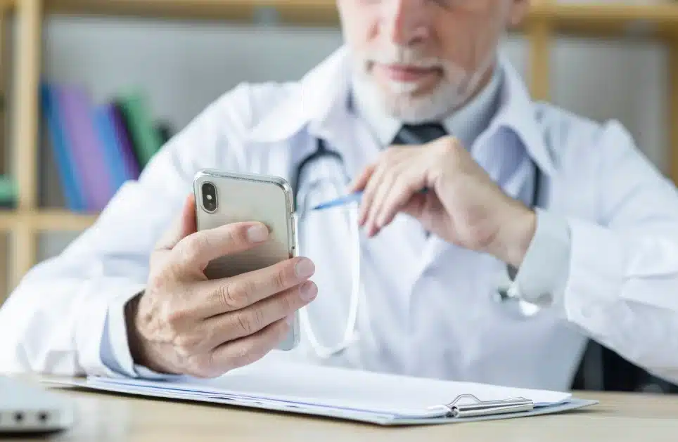 Médico usando un teléfono móvil mientras examina información relacionada con la salud, destacando la importancia de las aplicaciones de salud para profesionales médicos.