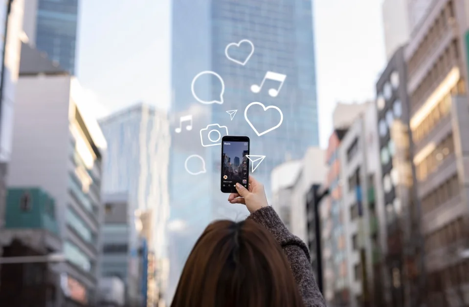 Persona tomando una foto con su teléfono móvil en una ciudad, rodeada de íconos de redes sociales flotando.